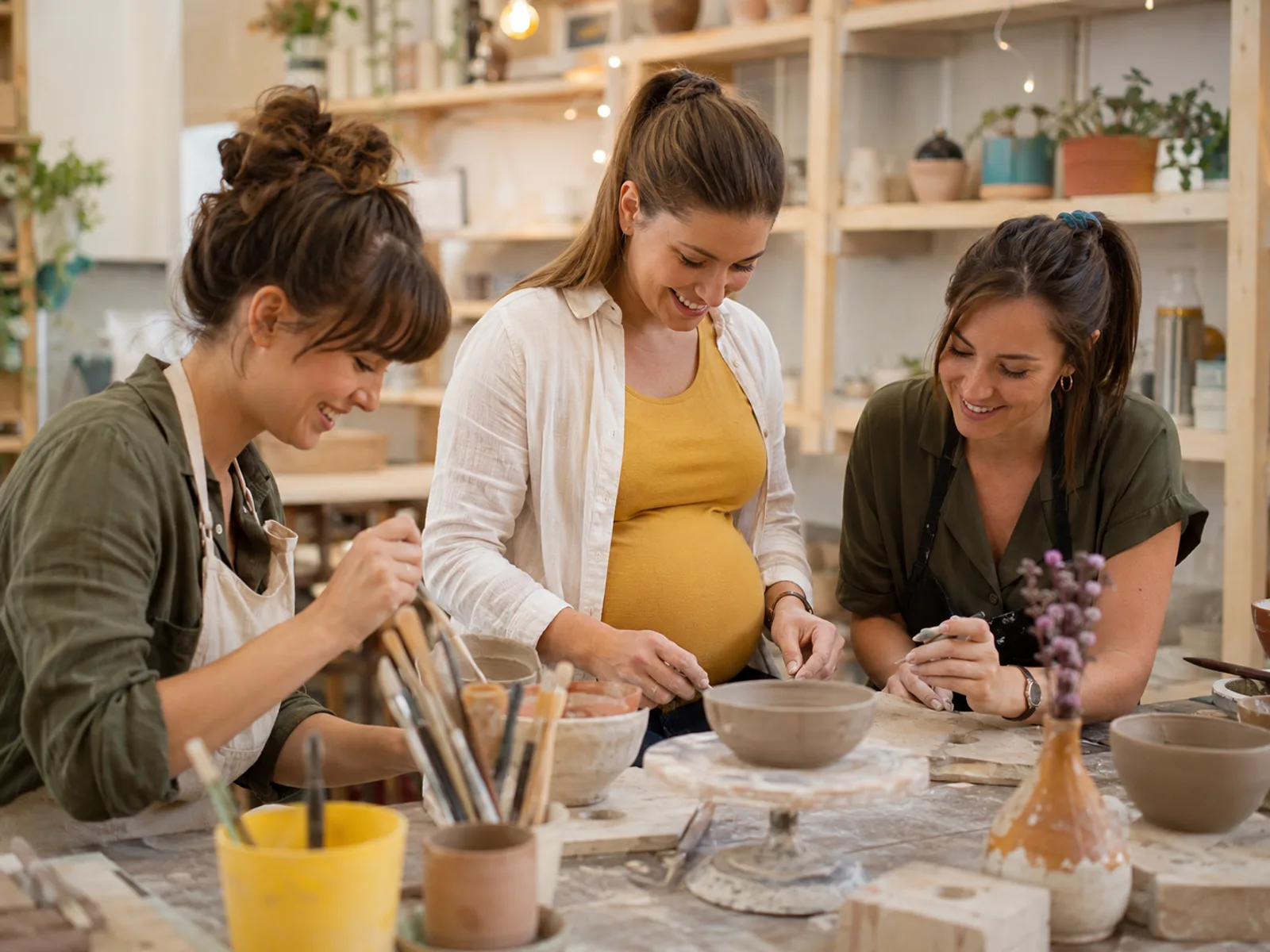 Gruppe von Frauen sitzt gemeinsam an einem Tisch und bemalt Keramik in einem Workshop